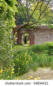 Archway Into An English Walled Garden With Irises Around A Pond