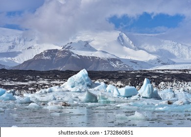 An arctic, polar scene with icebergs floating in Jokulsarlon Lagoon, a glacial lake located in the southern region of Iceland, with snow covered mountains and glaciers in the distance