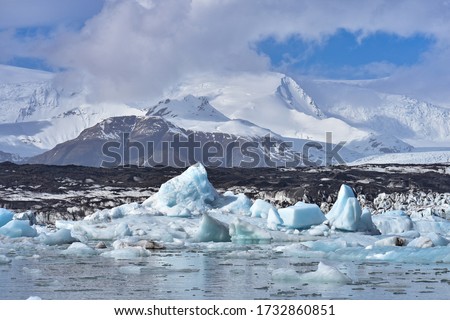 An arctic, polar scene with icebergs floating in Jokulsarlon Lagoon, a glacial lake located in the southern region of Iceland, with snow covered mountains and glaciers in the distance