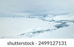 Arctic snow covered wild nature winter landscape. Aerial fly over polar ice ocean, frozen icebergs and mountains towering coastline in background. Antarctica travel and exploration. Low angle shot