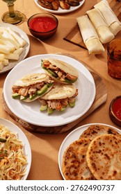 Arepas stuffed with pulled pork and avocado on white plate, surrounded by Latin American dishes. Traditional Venezuelan and Colombian street food concept.