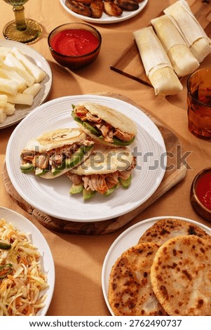 Arepas stuffed with pulled pork and avocado on white plate, surrounded by Latin American dishes. Traditional Venezuelan and Colombian street food concept.