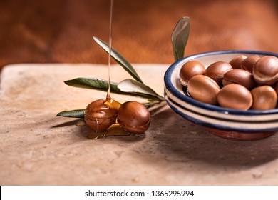 Argan oil, used for cosmetics, pouring over two argan seeds on a stone table.