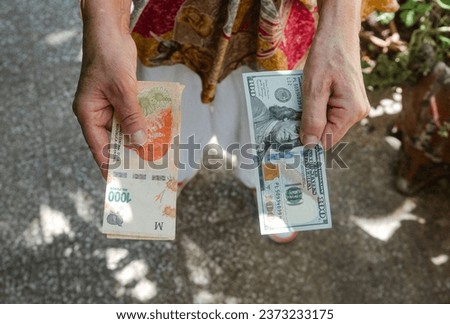 Argentine economic crisis concept. Woman holding argentine pesos and a 100 dollar bill. Inflation and rise of the dollar.