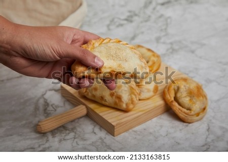 Argentinean Empanadas on a wooden board on a marble table. Hand holding an empanada.