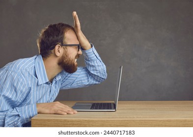 Argh, don't remember it. Side profile view angry ashamed guy slaps face sitting at office desk with laptop. Businessman makes stupid mistake online, forgets password, fails to fix computer malfunction - Powered by Shutterstock