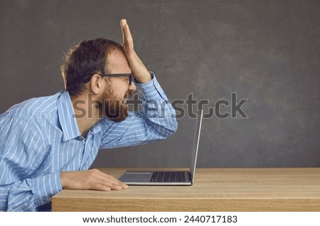 Argh, don't remember it. Side profile view angry ashamed guy slaps face sitting at office desk with laptop. Businessman makes stupid mistake online, forgets password, fails to fix computer malfunction