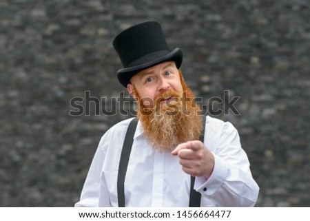 Argumentative talkative man in old fashioned top hat and braces pointing at the camera as he makes a point with persuasive expression over a grey background