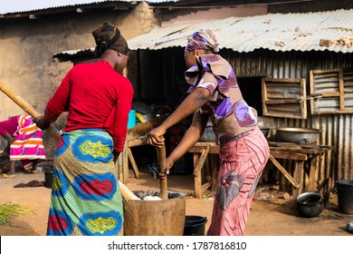 Argungu, Kebbi State, Nigeria - March 2020: Two Young Women Pounding Yam In A Mutter Together