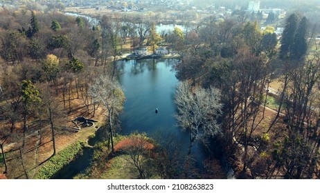 Arial Drone View Flight Over Lake In Park On Sunny Autumn Day. Flying Over Surface Of Water, Trees Fallen Leaves And Walking People In Public City Park Area. Urban Landscape With Architecture Fountain