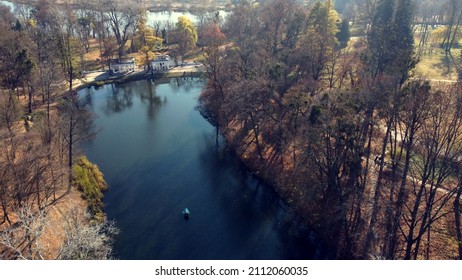 Arial Drone View Flight Over Lake In Park On Sunny Autumn Day. Flying Over Surface Of Water, Trees Fallen Leaves And Walking People In Public City Park Area. Urban Landscape With Architecture Fountain