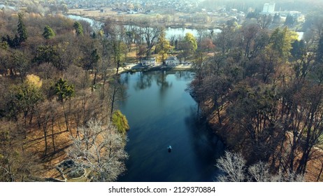 Arial Drone View Flight Over Lake In Park On Sunny Autumn Day. Flying Over Surface Of Water, Trees Fallen Leaves And Walking People In Public City Park Area. Urban Landscape With Architecture Fountain