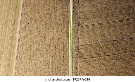 Arial Drone View Of Freshly Plowed Field Ready For Seeding And Planting In Spring. Dirty Road On Farmland. Empty Plowed Farm Land Prepared For The New Crop. Agriculture. Brown Black Soil Near Village.