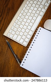 An Arial View Of An  IMac Wireless Keyboard, Mouse, Pen, And Desk Pad On An Oak Wood Desk