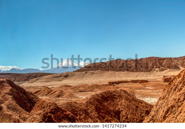 Arid landscape in\
extreme dry desert of Atacama : Moonlike landscape of dunes, rugged\
mountains and distinctive rock formations of Valle de la Luna (Moon\
valley), Northern Chile