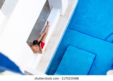 Ariel Shot Of An Attractive And Athletic Young Man Relaxing Next To A Swimming Pool Texting Or Using A Cellphone Or Mobile Phone On A Luxuary Holiday Or Vacation In Mexico