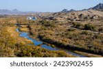 An Arizona desert river near the town of Yuma, with mountains in the background, plants and trees along the riverbank, in Yuma County, near the border with Mexico, in February of 2024.