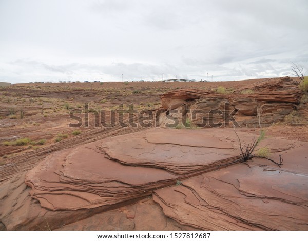 Arizona red desert landscape scenic view\
near Lake Powell, cloudy day, red rock strata, layered red rock\
formation in foreground, distant cars on the\
parking