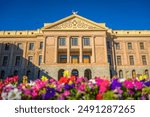 Arizona State Capitol in Phoenix, AZ, with colorful flowers in the foreground under a blue sky. It was the last home for Arizona