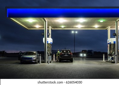 ARIZONA, USA - DECEMBER 22, 2016: Night Scene Of Gas Station Lit With Blue Light, Truck With Headlights On In The Background. Two Cars Parked By The Self-service Fuel Pump, Man Filling Up His Car.