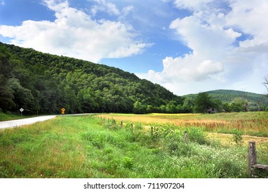 Arkansas Highway Curves And Disappears Around An Ozark Mountain.  Rustic Barn And Wooden Fence Sit Besides Highway.