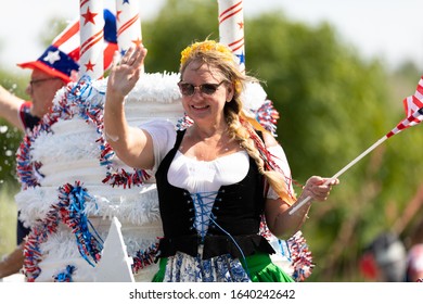 Arlington, Texas, USA - July 4, 2019: Arlington 4th of July Parade, Woman on float wearing german style traditional dress, waving the American flag at the parade