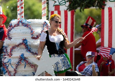 Arlington, Texas, USA - July 4, 2019: Arlington 4th of July Parade, Woman on float wearing german style traditional dress, waving the American flag at the parade