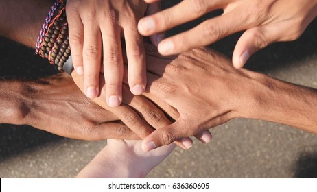 Arm of all races and colors stacked together one by one in unity and teamwork and then raised. Many multiracial hands getting together in the center of a circle and then cheer. Close up outdoor shot.