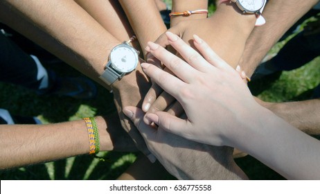 Arm Of All Races And Colors Stacked Together One By One In Unity And Teamwork And Then Raised. Many Multiracial Hands Getting Together In The Center Of A Circle And Then Cheer. Close Up Outdoor Shot.