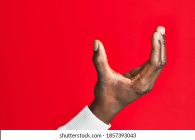 Arm and hand of african american black young man over red isolated background picking and taking invisible thing, holding object with fingers showing space 