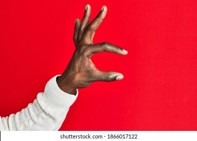 Arm and hand of african american black young man over red isolated background picking and taking invisible thing, holding object with fingers showing space 