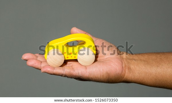 arm and hand of an\
African American man holding a yellow toy car in his palm against a\
solid background