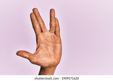 Arm And Hand Of Black Middle Age Woman Over Pink Isolated Background Greeting Doing Vulcan Salute, Showing Hand Palm And Fingers, Freak Culture 