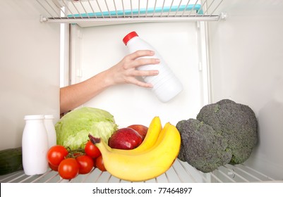 Arm inside refrigerator full of fruit and vegetables.