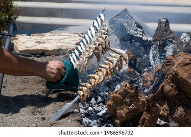 Arm Of A Man Catching A Skewer Of Sardines Over Incandescent And Smoky Embers