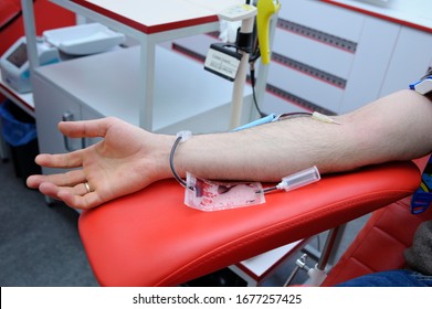 Arm On An Armrest, Hypodermic Needle, Tubes, Container With Blood. Taking Blood From The Vain Of A Donor