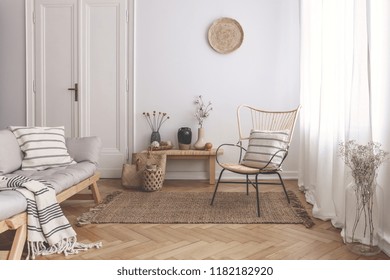 Armchair on rug next to bench with plants in white loft interior with wooden sofa. Real photo - Shutterstock ID 1182182920