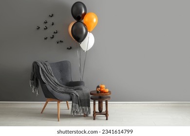 Armchair, table, Halloween balloons and bats hanging on grey wall in room