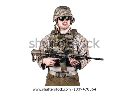 Armed american soldier with funny face looking somewhere holding his tactical battle rifle with both hands. He wears tactical military brown uniform and special vest. Isolated, white background.