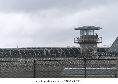 An armed guard surveys the grounds from the railing of a prison watchtower