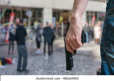 Armed man (attacker) holds pistol in public place. Many people on street. Gun control concept.