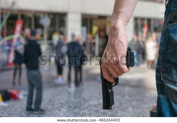 Armed man (attacker) holds pistol in\
public place. Many people on street. Gun control\
concept.