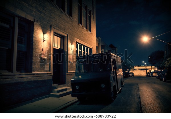 An armed security truck parked in a\
dark city street at night next to a building\
entrance.