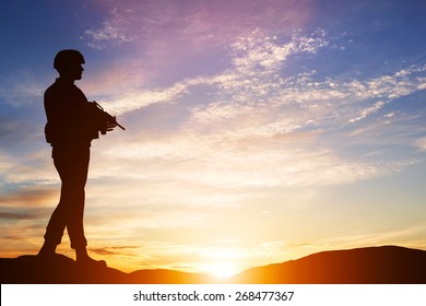 Armed Soldier With Rifle Standing And Looking On Horizon. Silhouette At Sunset. War, Army, Military, Guard.