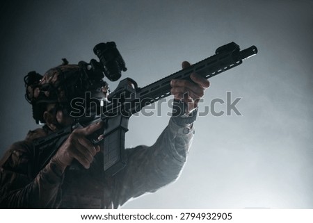 Armed special forces serviceman in camouflage uniform using optical sight, studio portrait for surveillance, security and military strategy themes