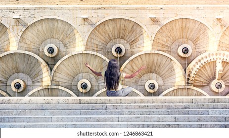 Armenian brunette girl with long hair sits on the stairs and stretch her arms for meditation. Back view