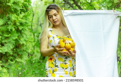 An Armenian girl standing next to hung laundry in a yard with a transparent bowl of lemons in her hand, looking to the side