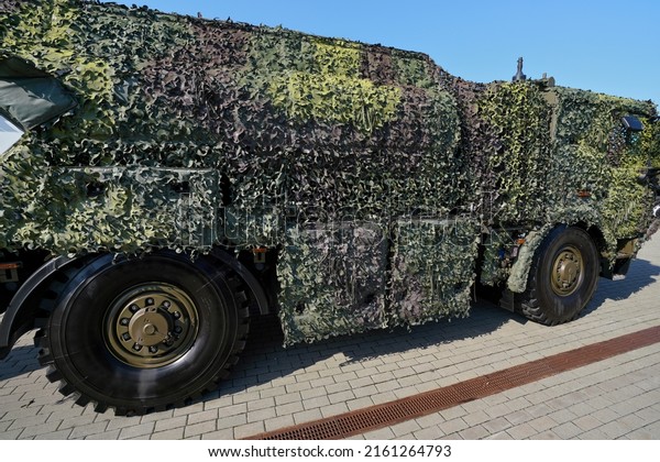 Armoured truck\
completely covered with camouflage mesh net parked at pavement on\
sunny day, side view