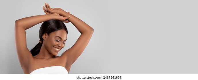 Armpit Depilation Concept. Happy Black Lady Looking At Her Smooth Underarms, Smiling African American Woman Wrapped In Towel After Bath Standing With Hands Up Over Gray Studio Background, Copy Space - Powered by Shutterstock