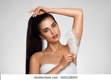 Armpit epilation, hair removal. Young woman holding her arms up and showing clean underarms, depilation smooth clear skin . Beauty portrait. armpit's care. Large white feather near skin - Powered by Shutterstock